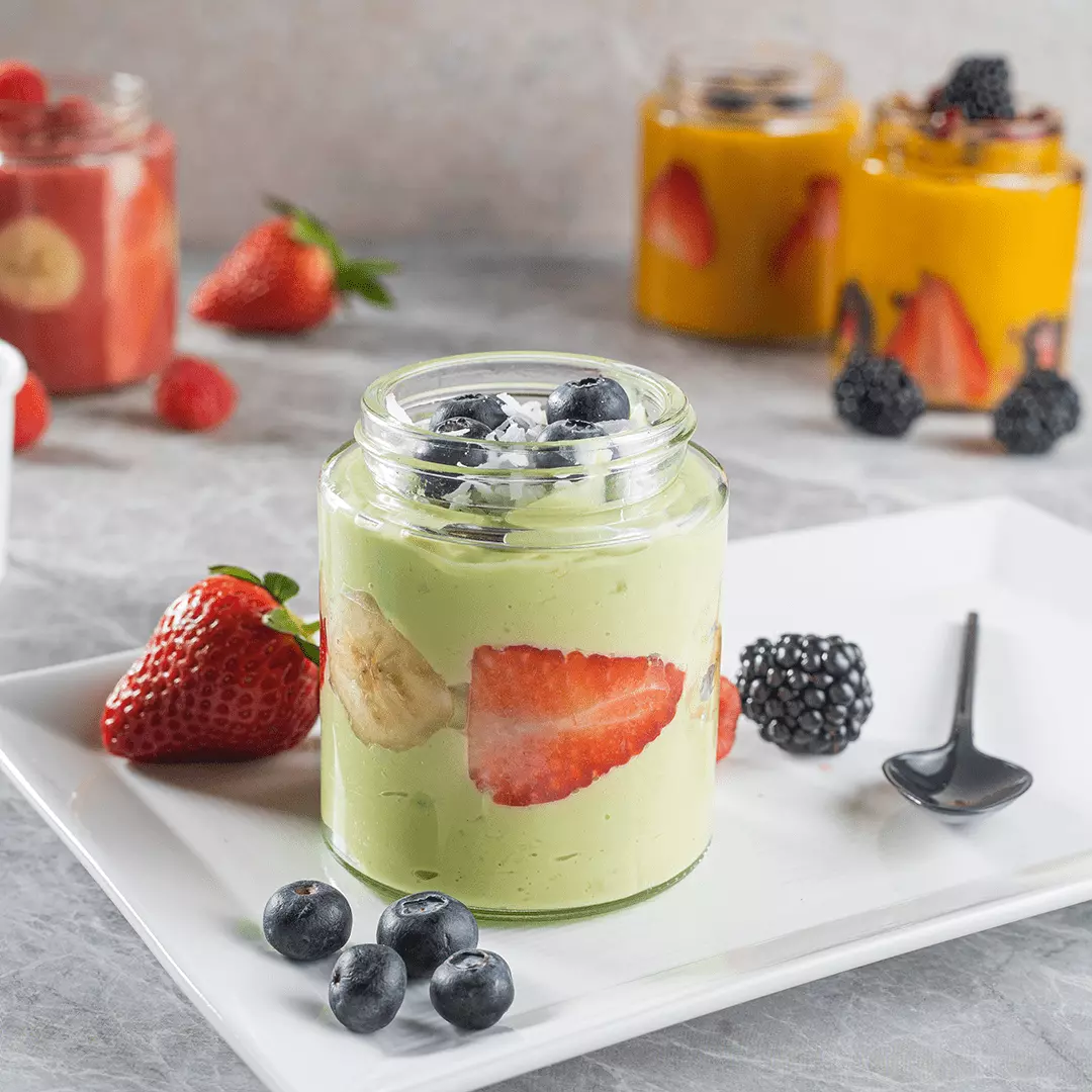 A jar containing milkshake on a plate with a spoon and other jars in the background